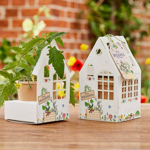 Deux petits paquets en forme de maison étiquetés « Finn's Sweet Garden », l'un contenant une plante en pot, avec des fleurs floues et un mur de briques en arrière-plan.