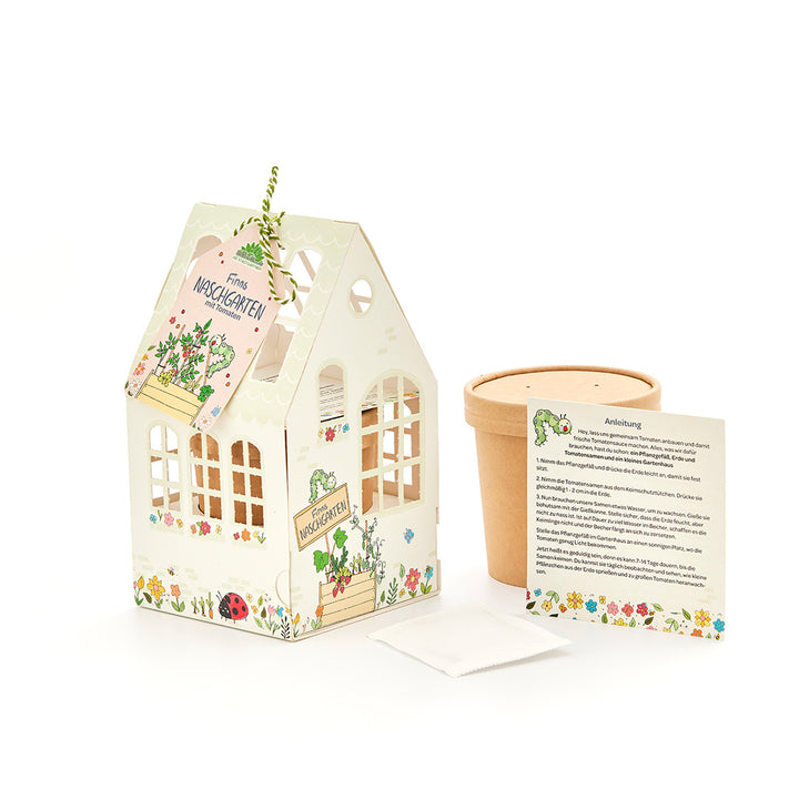 Coffret comprenant une petite serre décorative, un pot de fleurs, des instructions et un sachet de graines pour faire pousser des tomates.