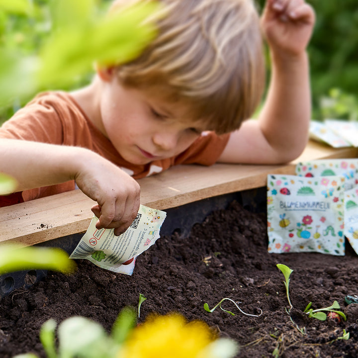 Un garçon plante des graines dans un parterre de jardin tout en tenant un sac de graines.