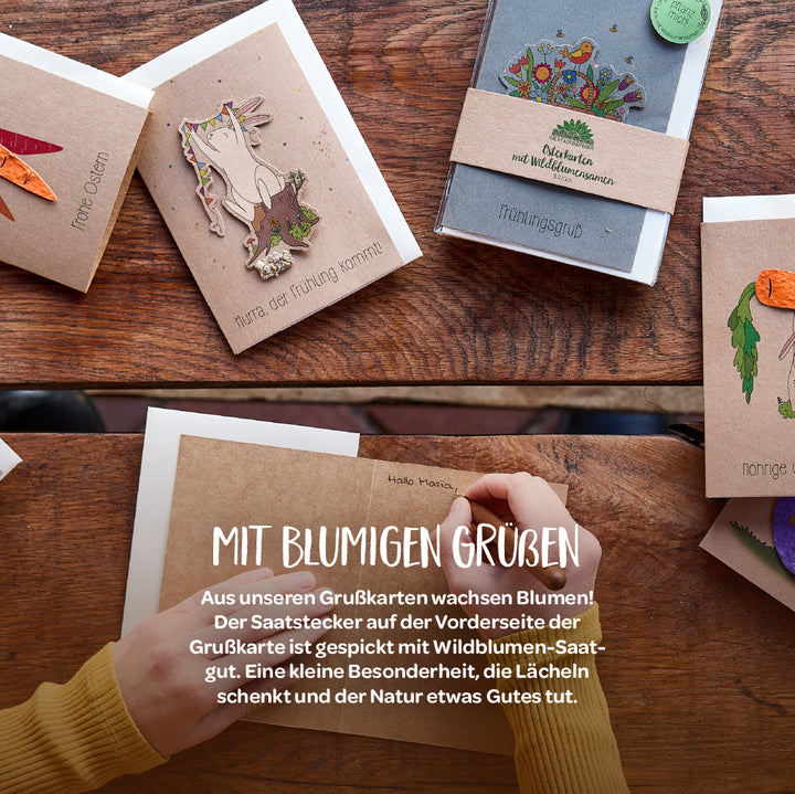 Plusieurs cartes de vœux colorées avec des motifs et des textes de printemps et de Pâques sont posées sur une table en bois ; une personne écrit une carte.