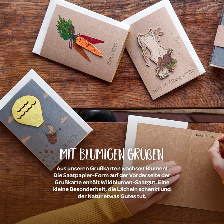 Diverses cartes de vœux avec des motifs décoratifs en papier ensemencé sur une table en bois, notamment des carottes, un lapin et une montgolfière.