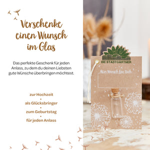 Image publicitaire pour un concept cadeau « Wish in a Jar » avec du texte, un verre sur une carte et des fleurs séchées en arrière-plan.