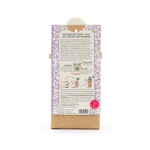 Dos d'un emballage avec un motif floral violet, un texte sur le caractère écologique de l'arbre Kiri, des instructions de plantation et le logo du Seed Festival en bas à droite.