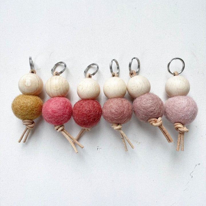 Ensemble de porte-clés faits main avec boules de feutre de laine et perles en bois sur fond blanc.