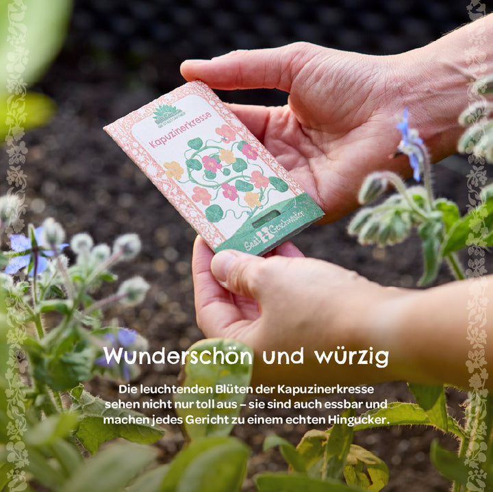 Mains tenant un sachet de graines étiqueté « capucine » dans le jardin, avec des plantes à fleurs à côté.