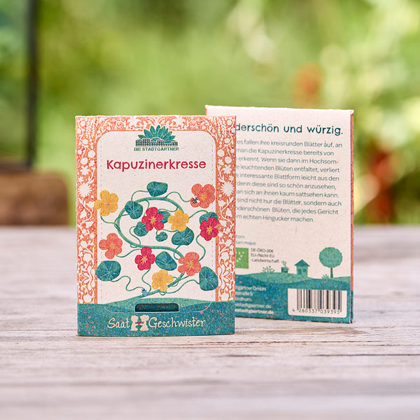 Deux sachets de graines de capucine avec une illustration colorée sur une table en bois à l'extérieur.