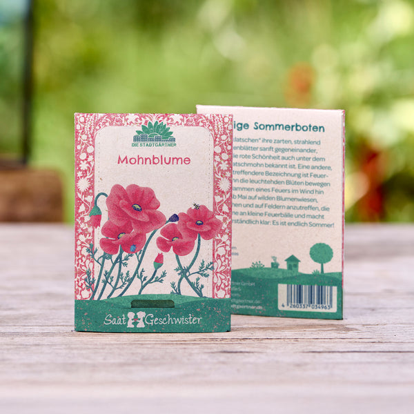 Deux sachets de graines de pavot avec des fleurs rouges illustrées sur un fond en bois et un arrière-plan de jardin flou.