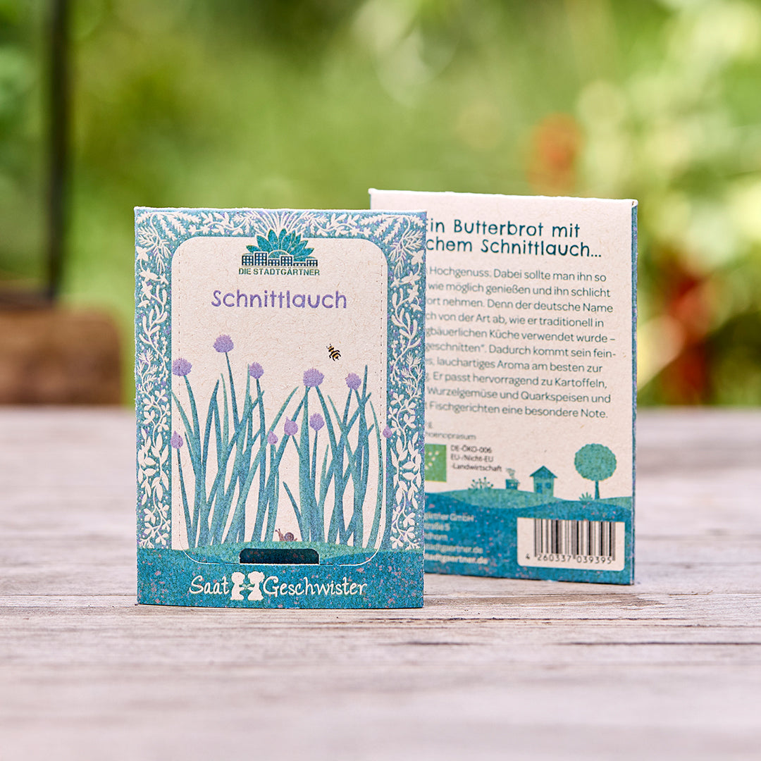Deux sachets de graines de ciboulette de « Die Stadtgärtner » sur une table en bois, avec un fond vert flou.