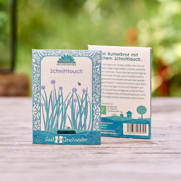 Deux sachets de graines de ciboulette de « Die Stadtgärtner » sur une table en bois, avec un fond vert flou.