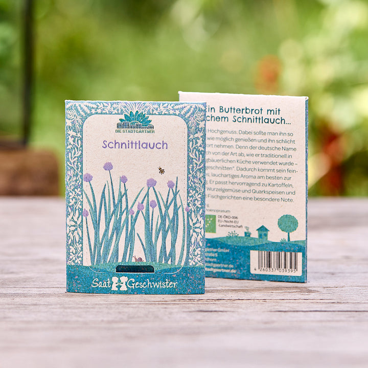 Deux sachets de graines de ciboulette de « Die Stadtgärtner » sur une table en bois, avec un fond vert flou.