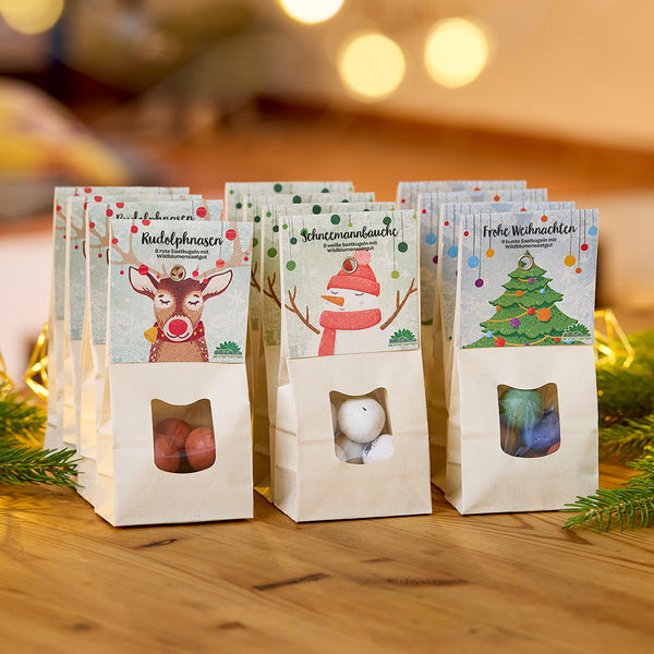 Trois sacs de bonbons décorés pour Noël sur une table en bois, chacun étiqueté « Nez de Rudolph », « Ventre de bonhomme de neige » et « Joyeux Noël ».