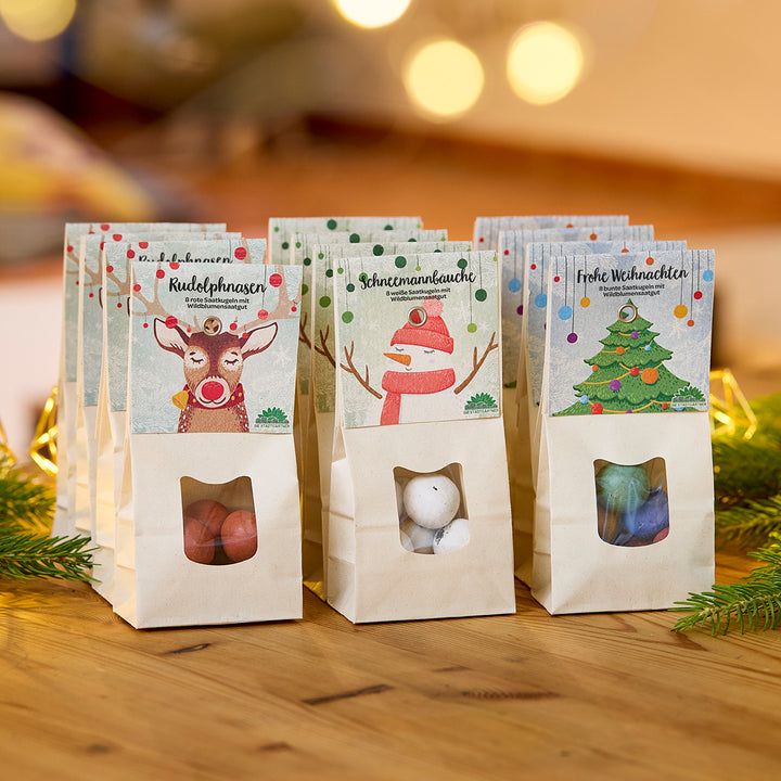 Trois sacs en papier décorés pour Noël et remplis de bonbons, étiquetés « Nez de Rudolph », « Ventre de bonhomme de neige » et « Joyeux Noël », se trouvent sur une table en bois.