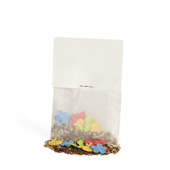 Petit sac en papier avec des biscuits colorés en forme de fleurs et d'animaux, dont certains sont tombés, sur un fond blanc.