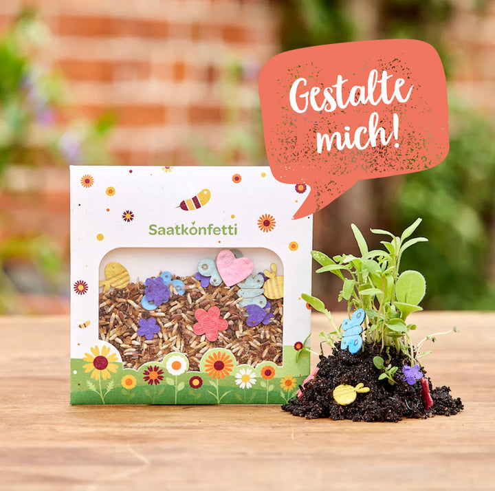Paquet de confettis de graines et de petites figurines en papier colorées, à côté de jeunes plantes, sur une table en bois, avec une nature floue en arrière-plan.