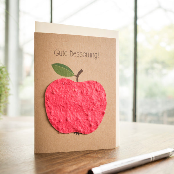 Carte de voeux avec le texte "Bon rétablissement !" et une pomme rouge sur une table en bois.