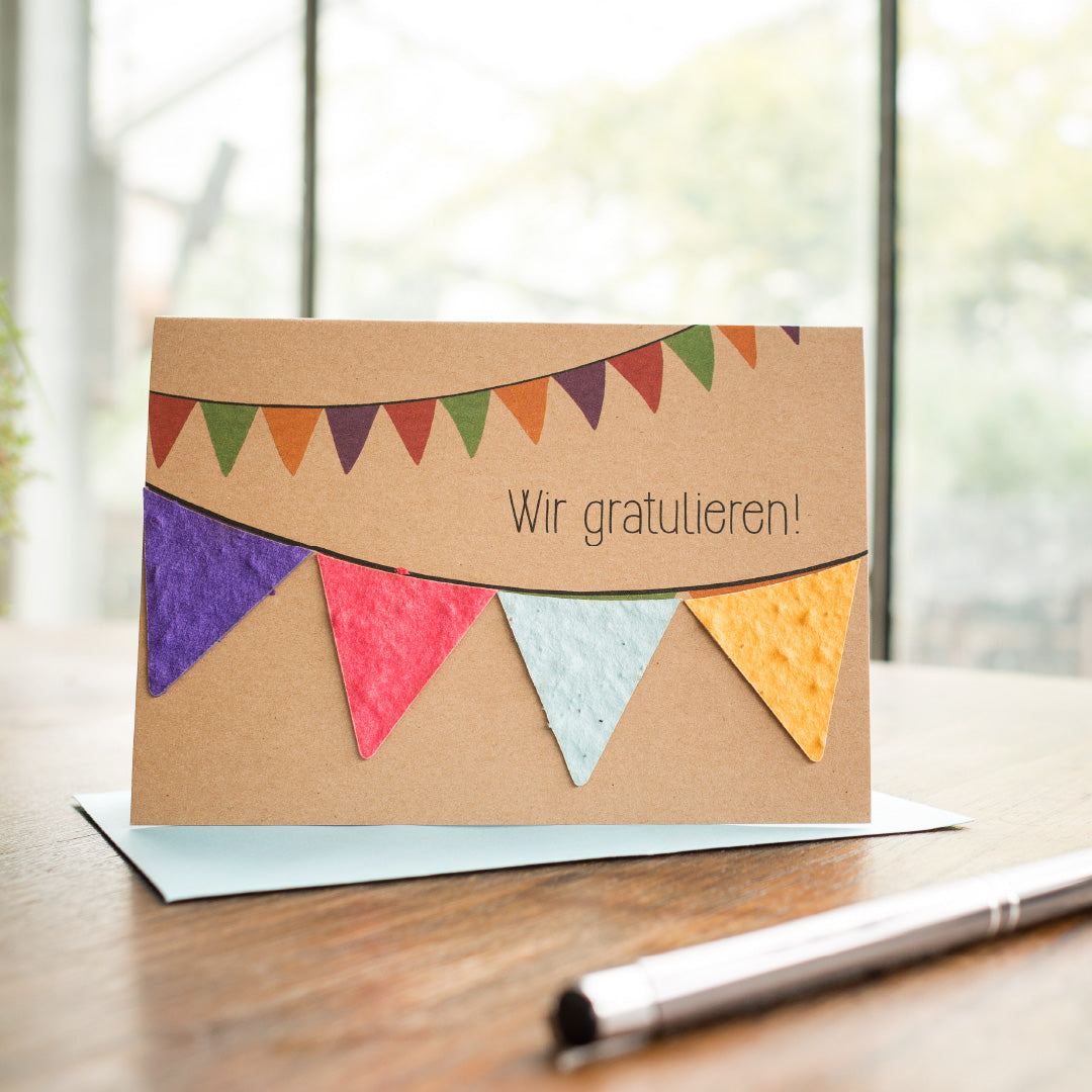 Carte de voeux avec l'inscription "Félicitations !" et des fanions colorés sur une table en bois avec un stylo et une enveloppe.
