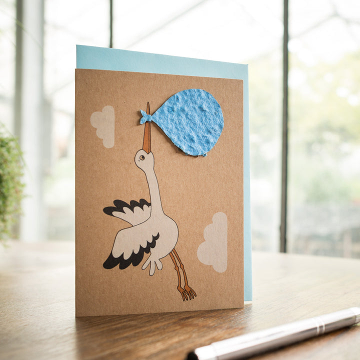 Carte de vœux faite à la main avec une cigogne portant un paquet bleu sur une table avec un stylo.
