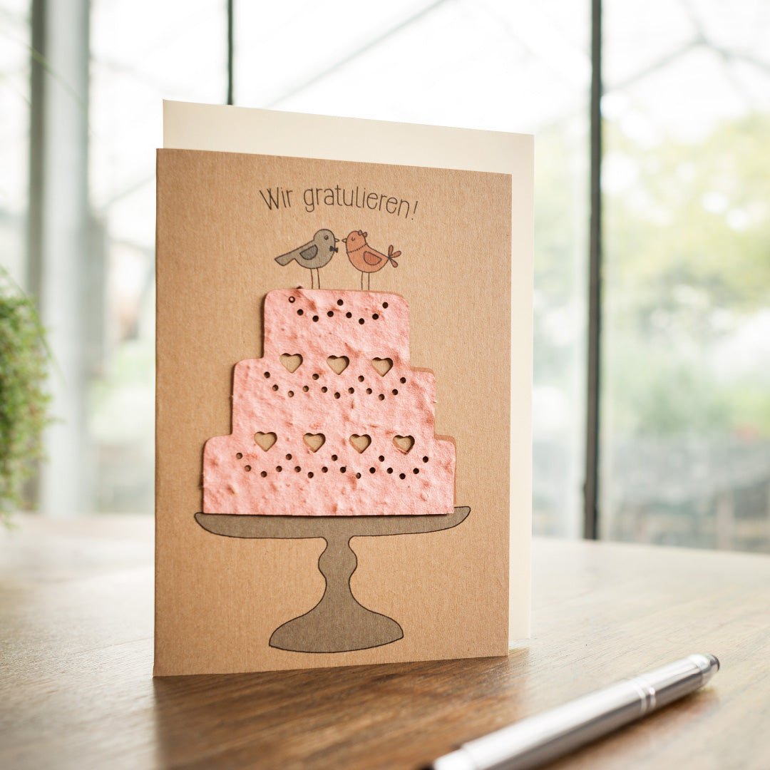 Carte de voeux avec un gâteau rose et deux oiseaux, avec le texte "Félicitations !" ci-dessus.
