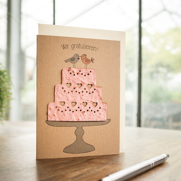 Carte de voeux avec un gâteau rose et deux oiseaux, avec le texte "Félicitations !" ci-dessus.