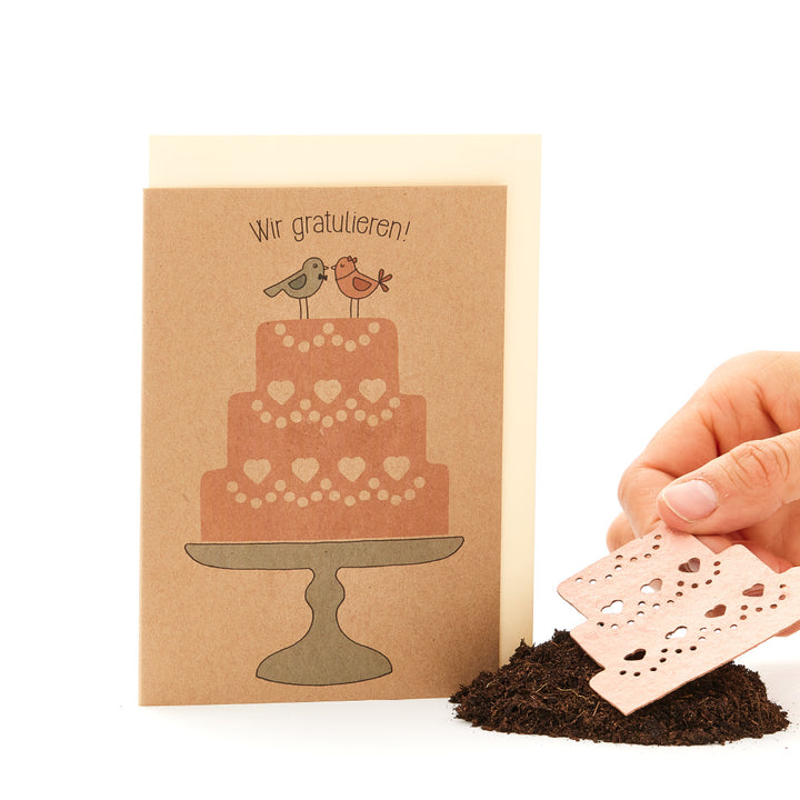Carte de voeux avec un gâteau imprimé et deux oiseaux ainsi qu'une main humaine tenant un morceau de papier.