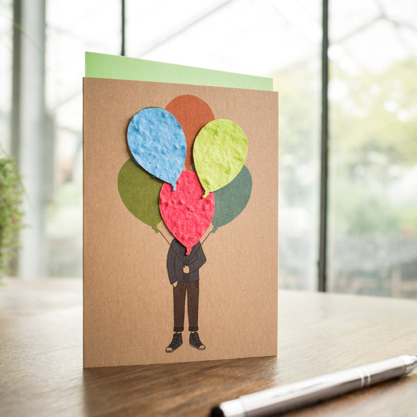 Carte de voeux avec illustration d'une personne dont la tête est faite de ballons en papier colorés, sur une table à côté d'un stylo.