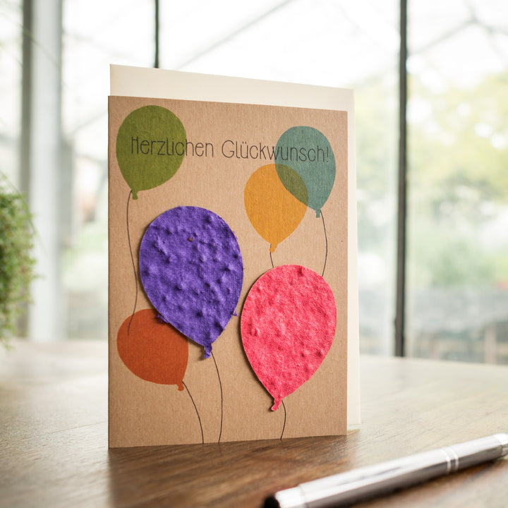 Carte de voeux avec des ballons colorés et les mots « Félicitations ! » sur une table en bois.