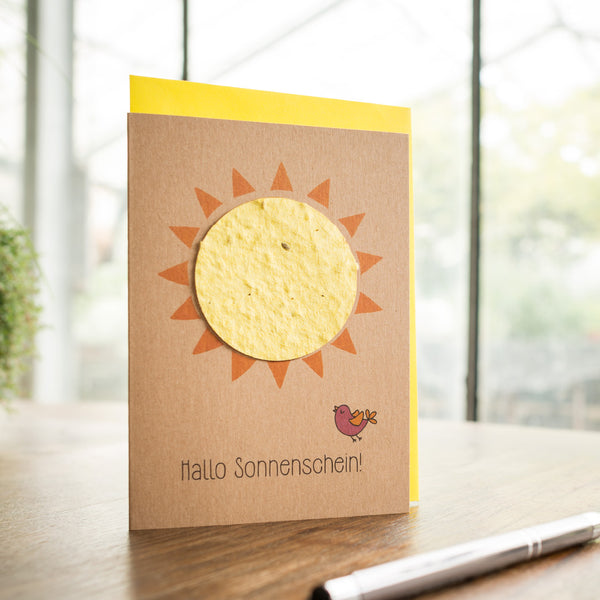Carte de vœux faite à la main avec un soleil et l'inscription "Hello Sunshine!" avec un petit oiseau sur une table en bois.