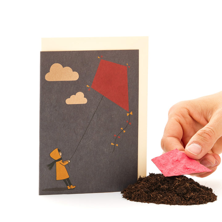 Main tenant une carte de vœux avec une illustration d'un enfant faisant voler un cerf-volant.
