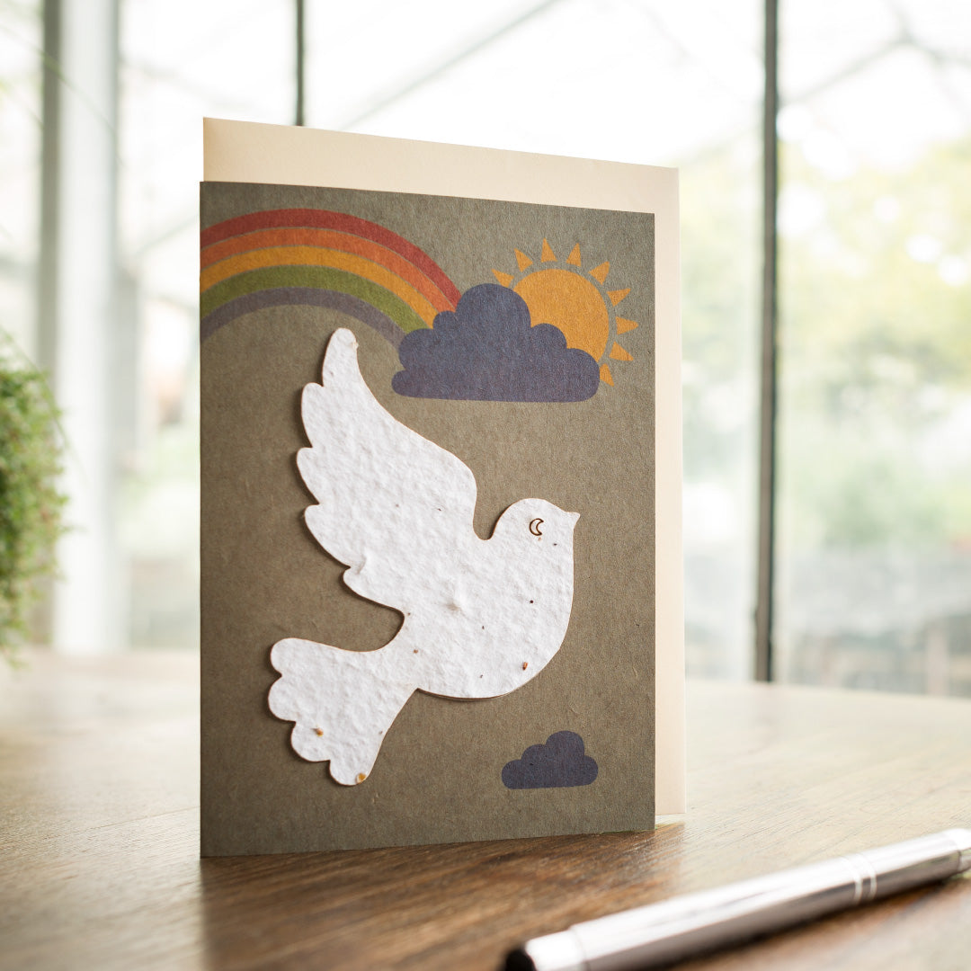 Carte de voeux avec colombe de la paix, arc-en-ciel et soleil sur une table.