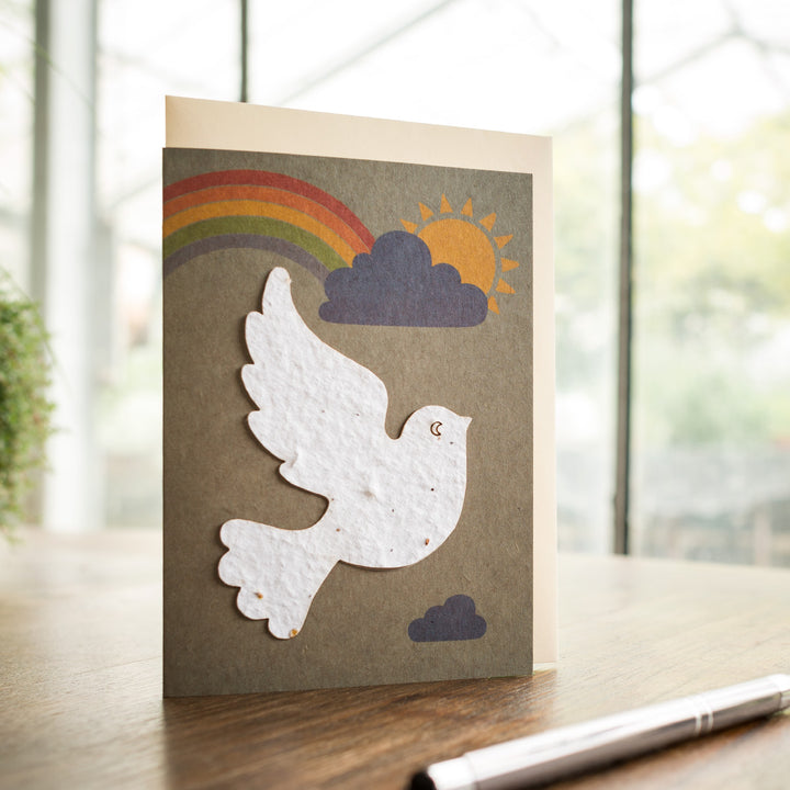 Carte de voeux avec colombe de la paix, arc-en-ciel et soleil sur une table.