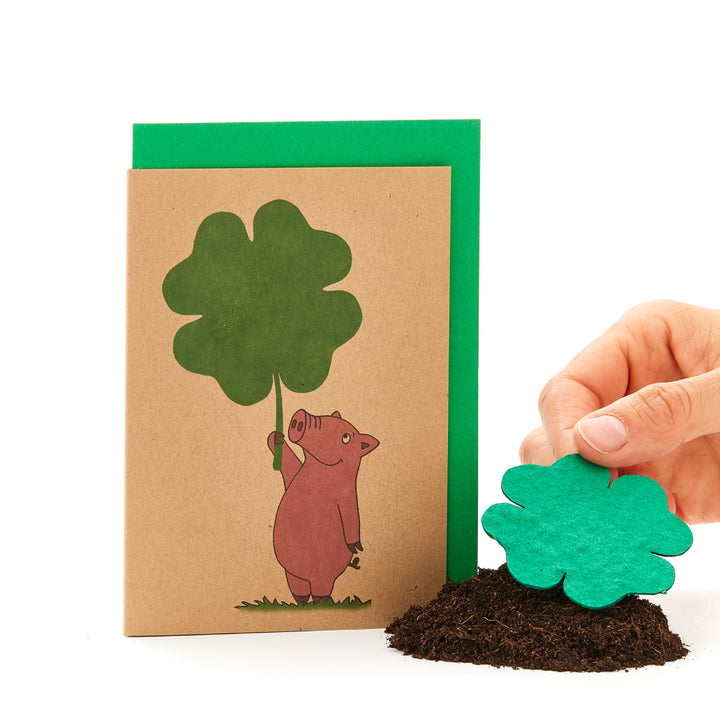 Main tenant une feuille de trèfle à côté d'une carte de vœux avec un cochon tenant une feuille de trèfle.