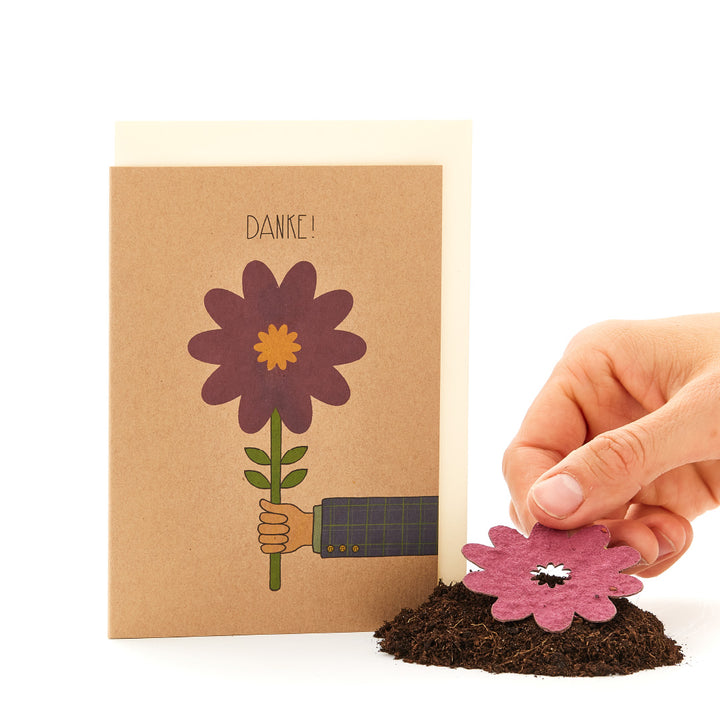 Main tenant une fleur en papier à côté d'une carte de remerciement avec une fleur dessinée.