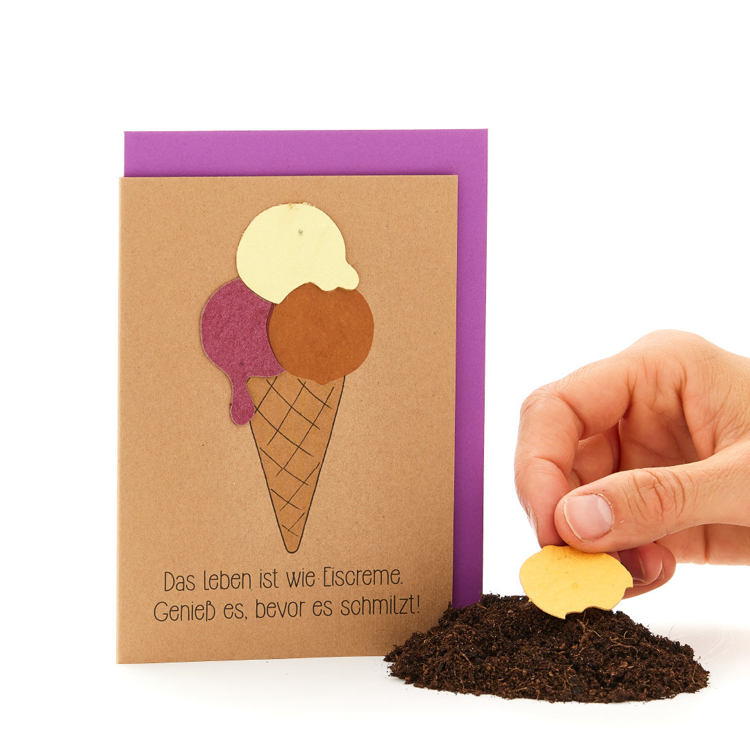 Main plantant un biscuit en forme de cœur dans la terre, à côté d'une carte de vœux en forme de cornet de glace avec le slogan : « La vie est comme une glace. Savourez-la avant qu'elle ne fonde ! »