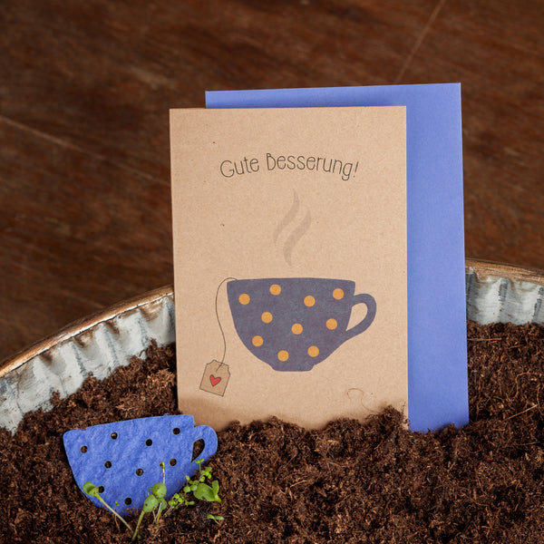 Carte de prompt rétablissement avec les mots « Bon rétablissement ! » et une tasse illustrée sur le devant, à côté d'un surmatelas en papier bleu en terre.