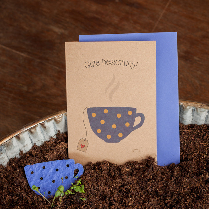 Carte de prompt rétablissement avec les mots « Bon rétablissement ! » et une tasse illustrée sur le devant, à côté d'un surmatelas en papier bleu en terre.