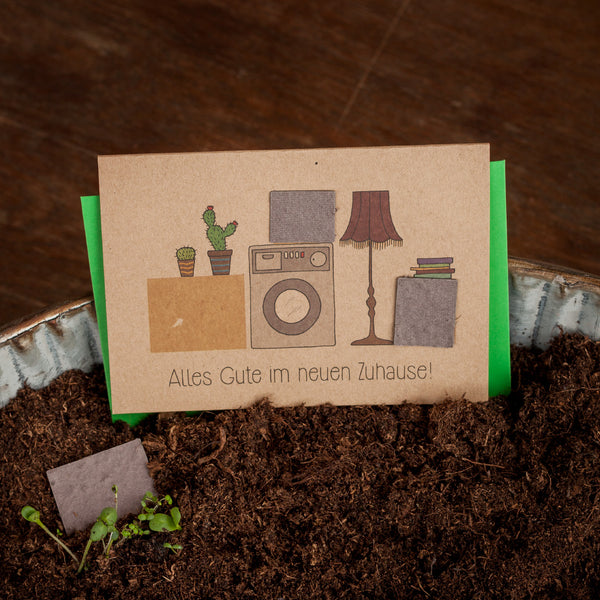 Carte de félicitations avec plantes en pot, machine à laver et lampe, texte : Tous mes vœux de bonheur dans votre nouvelle maison !