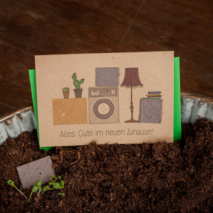 Carte de félicitations avec plantes en pot, machine à laver et lampe, texte : Tous mes vœux de bonheur dans votre nouvelle maison !