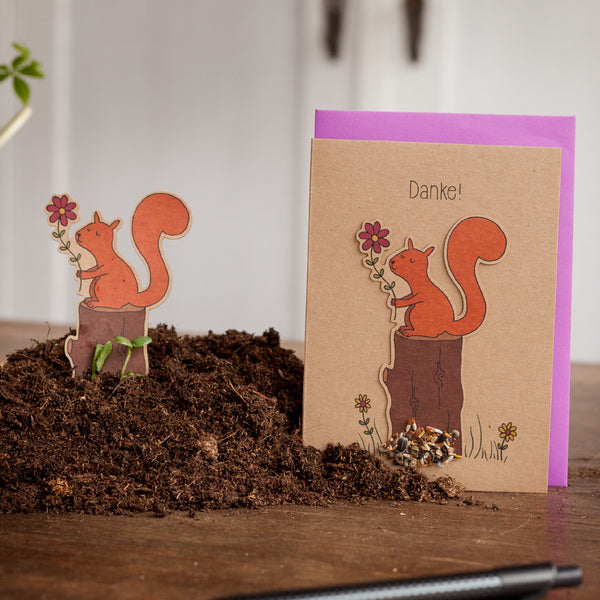 Carte de vœux avec un motif d'écureuil et le mot « Merci ! » dessus, à côté d'une figure d'écureuil découpée sur terre.