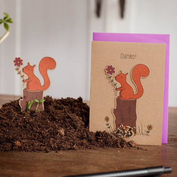 Carte de vœux avec un motif d'écureuil et le mot « Merci ! » dessus, à côté d'une figure d'écureuil découpée sur terre.