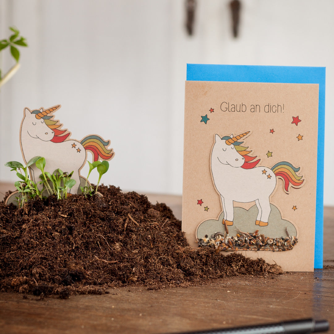 Une carte de vœux représentant une licorne et le texte « Croyez en vous ! » à côté d'une petite découpe de licorne entourée de terre.