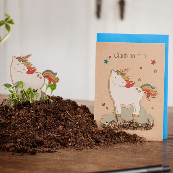 Une carte de vœux représentant une licorne et le texte « Croyez en vous ! » à côté d'une petite découpe de licorne entourée de terre.