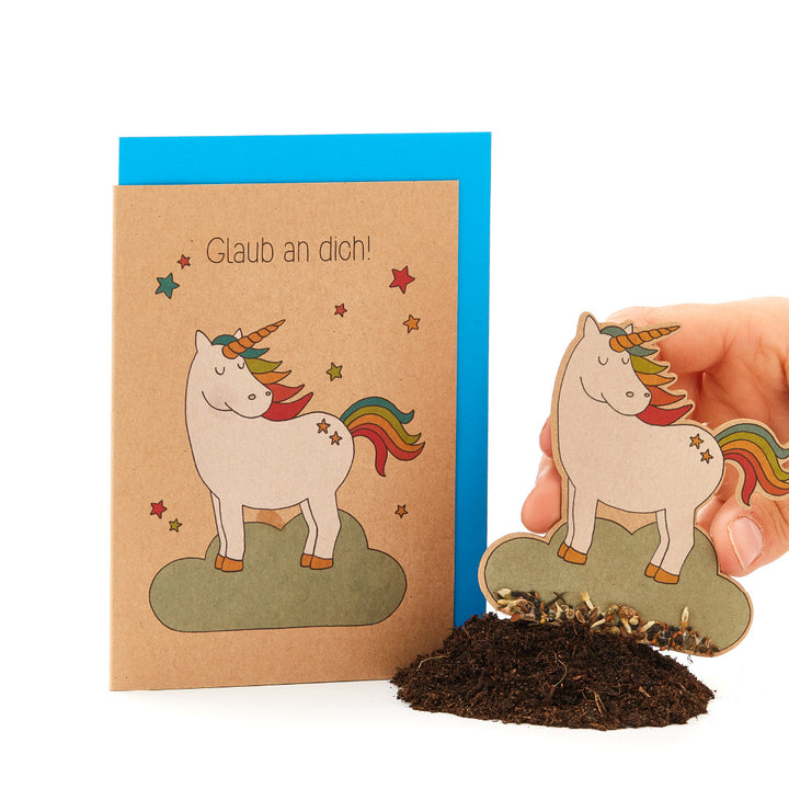 Carte de vœux avec une licorne et un arc-en-ciel, le texte « Croyez en vous-même ! » et une main plantant un papier licorne assorti dans le sol.