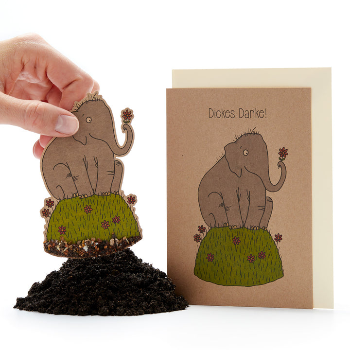 Main tenant un tableau de croissance de plante en forme d'éléphant à côté d'une carte de vœux sur laquelle est écrit « Un grand merci !