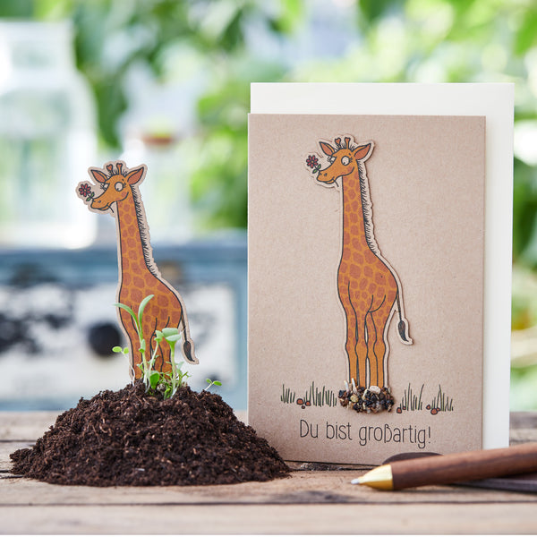 Carte de vœux avec un motif de girafe et les mots « Tu es génial ! » à côté d'un tas de terre et d'un crayon.