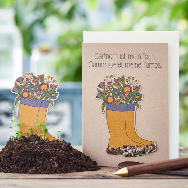 Carte de vœux avec le dicton « Le jardinage est mon yoga, les bottes en caoutchouc mes escarpins » et des bottes en caoutchouc illustrées remplies de fleurs sur un fond d'ustensiles de jardinage.