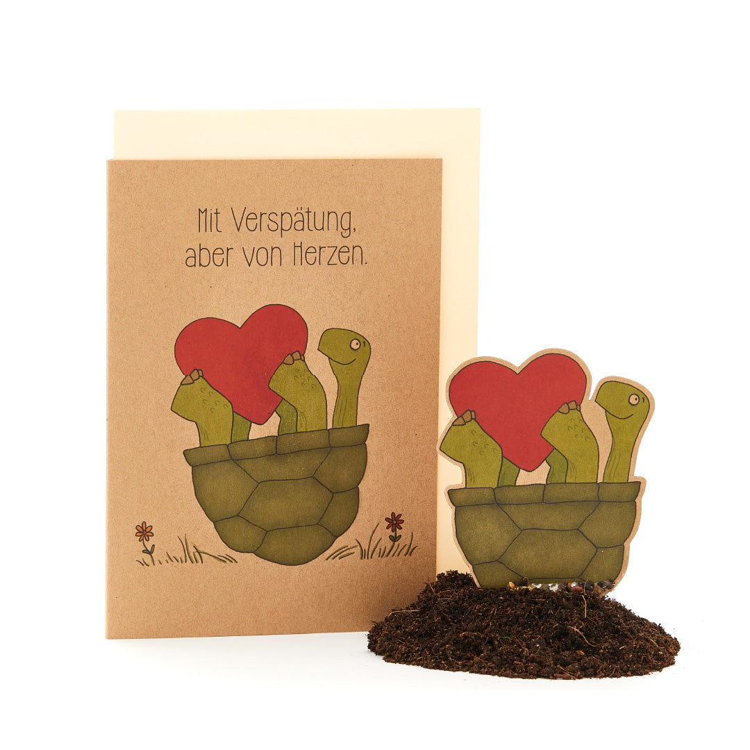 Carte de vœux avec le texte « En retard, mais du fond du cœur » et une illustration de plantes ressemblant à des cactus dans un pot portant des fleurs en forme de cœur.