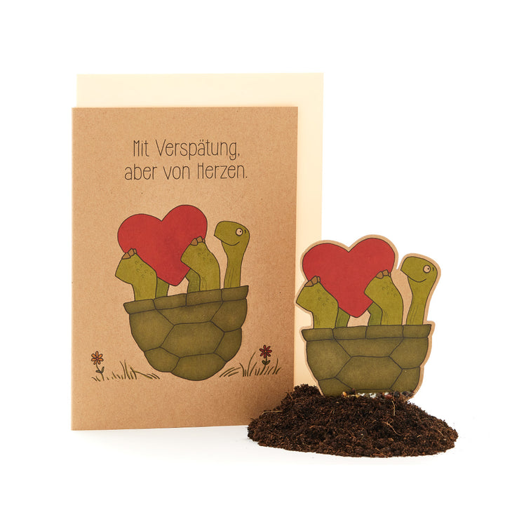 Carte de vœux avec le texte « En retard, mais du fond du cœur » et une illustration de plantes ressemblant à des cactus dans un pot portant des fleurs en forme de cœur.