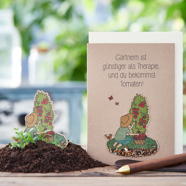 Une carte de vœux avec le dicton « Le jardinage est moins cher que la thérapie, et vous obtenez des tomates ! » à côté d'un tas de terre et d'une truelle de jardin.