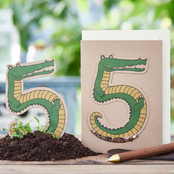 Représentation créative de nombres sous forme de crocodiles sur papier, à côté de terre et de crayon.