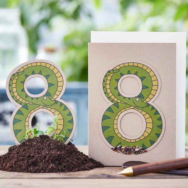 Carte de vœux créative avec le numéro 8 conçu comme un serpent sur terre avec un petit stylo à côté.